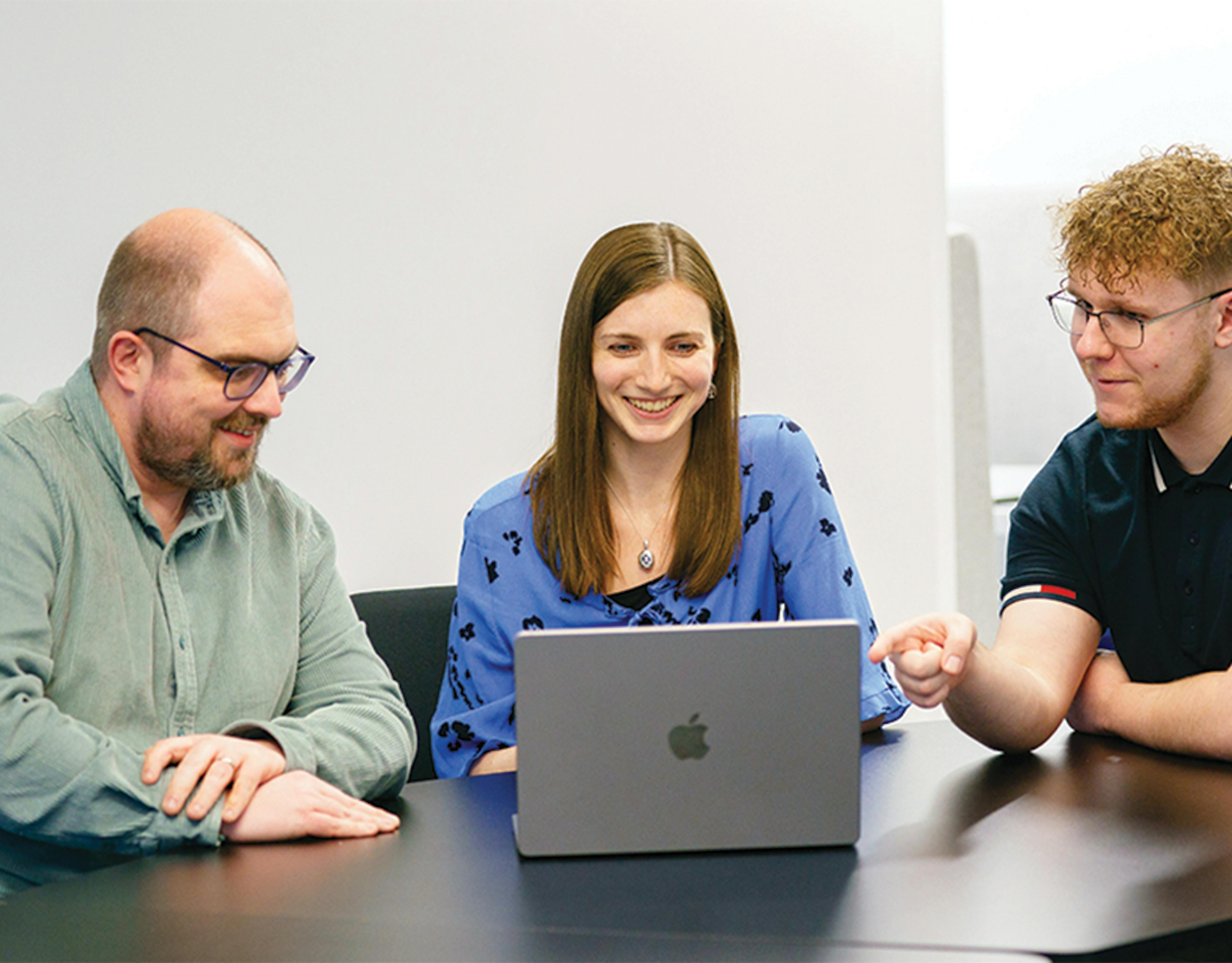 Three people at a desk around a laptop
